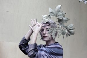 Lucilla Giagnoni, attrice, in un primo piano con il volto semi coperto da un ramo con foglie