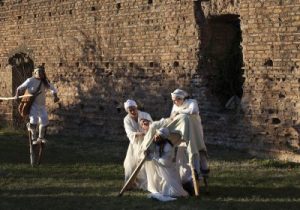 due donne che fanno scendere dai trampoli una terza, sullo sfondo una quarta donna sui trampoli si avvicina